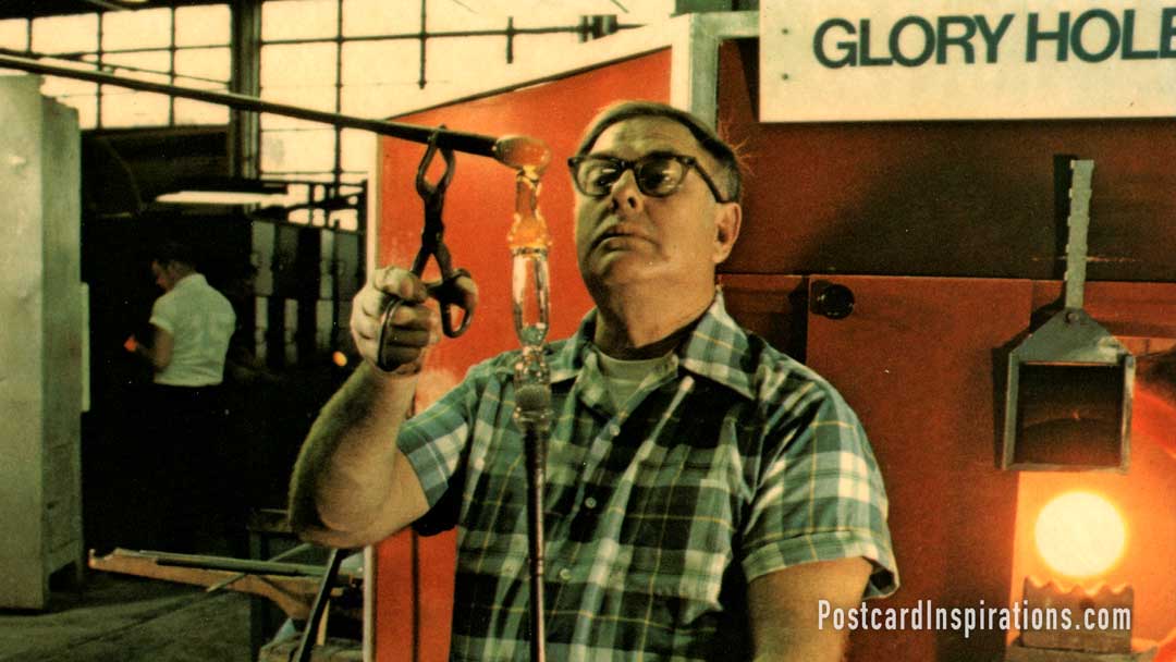 In the Steuben Glass Factory, a "gaffer "or master craftsman, as an extra gather of glass to make the foot of the wineglass. (Postcard)